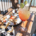 Colorful cocktail with lime garnish on a wooden table with food.