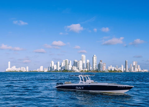 A dark blue and white speedboat with 'Charleroi, MI' written on its side, sailing on blue water with a Miami city skyline and a bright blue sky in the background.