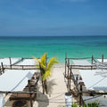 Beachside setup with white canopies, tables, and chairs under a clear blue sky.