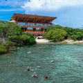 People swimming in clear blue water near Pao Pao with a wooden building.